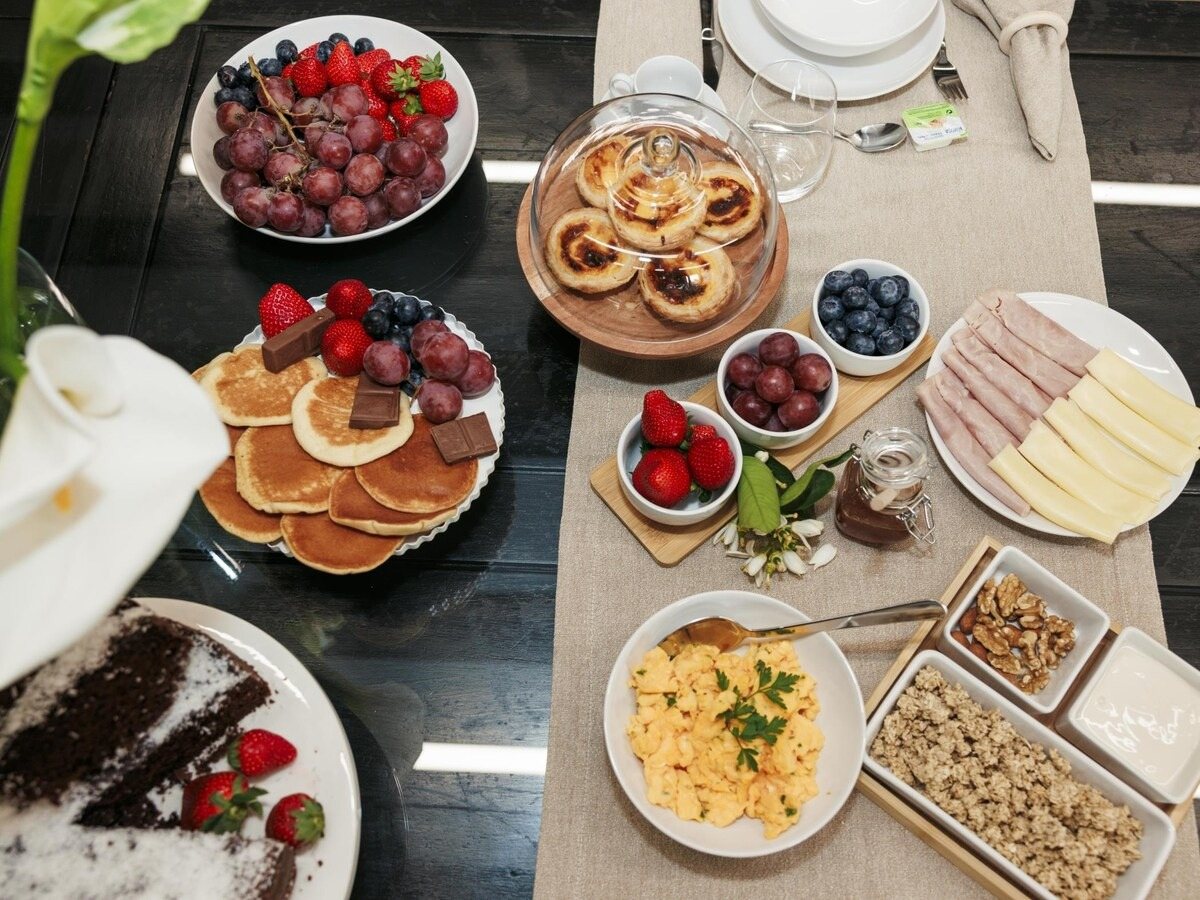 Mesa de pequeno-almoço com fruta, panquecas e pastéis de nata